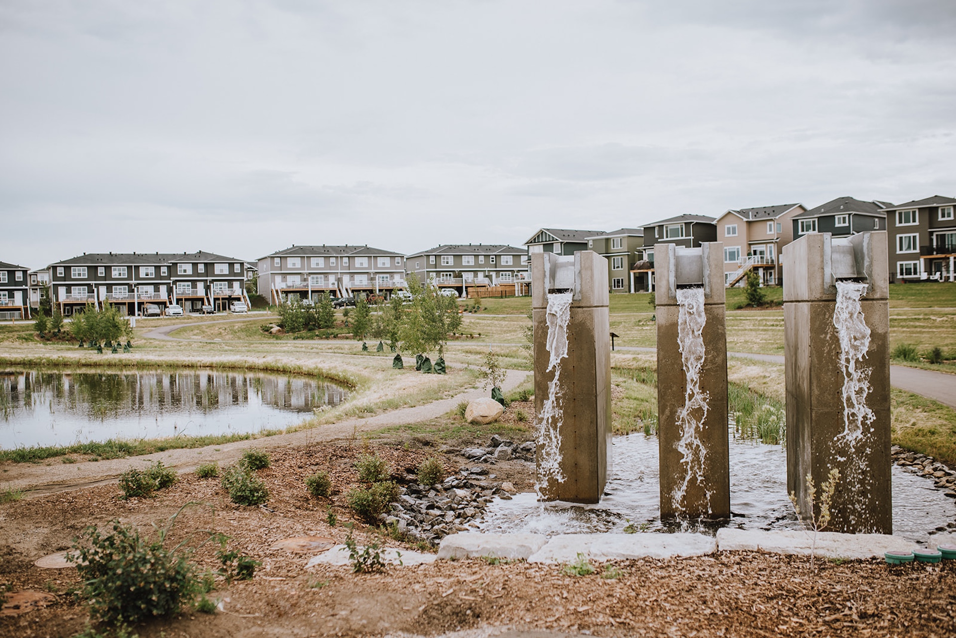 Three tall concrete pillars with water flowing from metal spouts into a pond, set in Dawson's Landing.