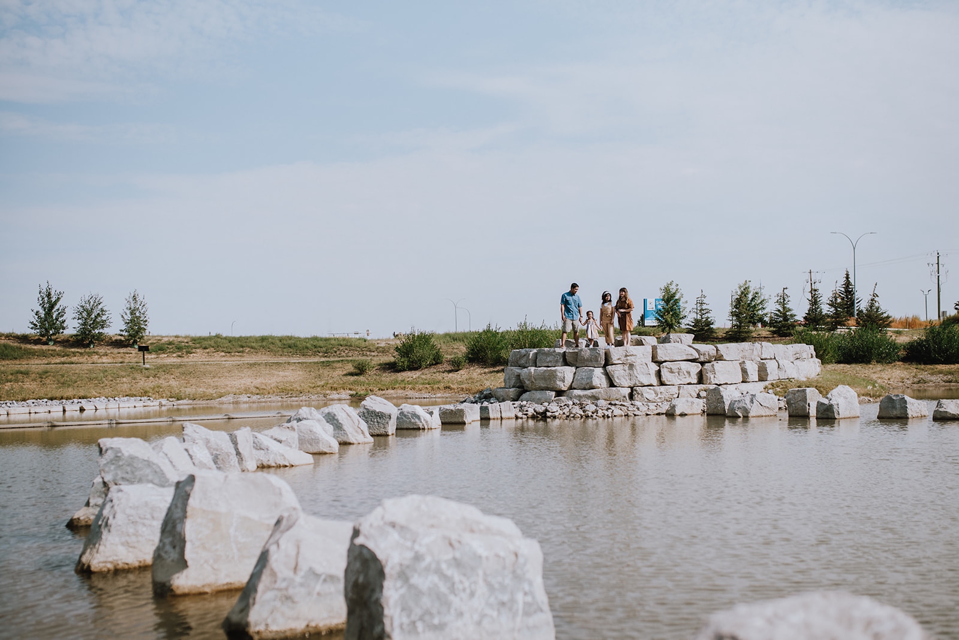 Family in Dawson's Landing standing on a stone platform surrounded by a lake, with large boulders creating a partial circle in the water.