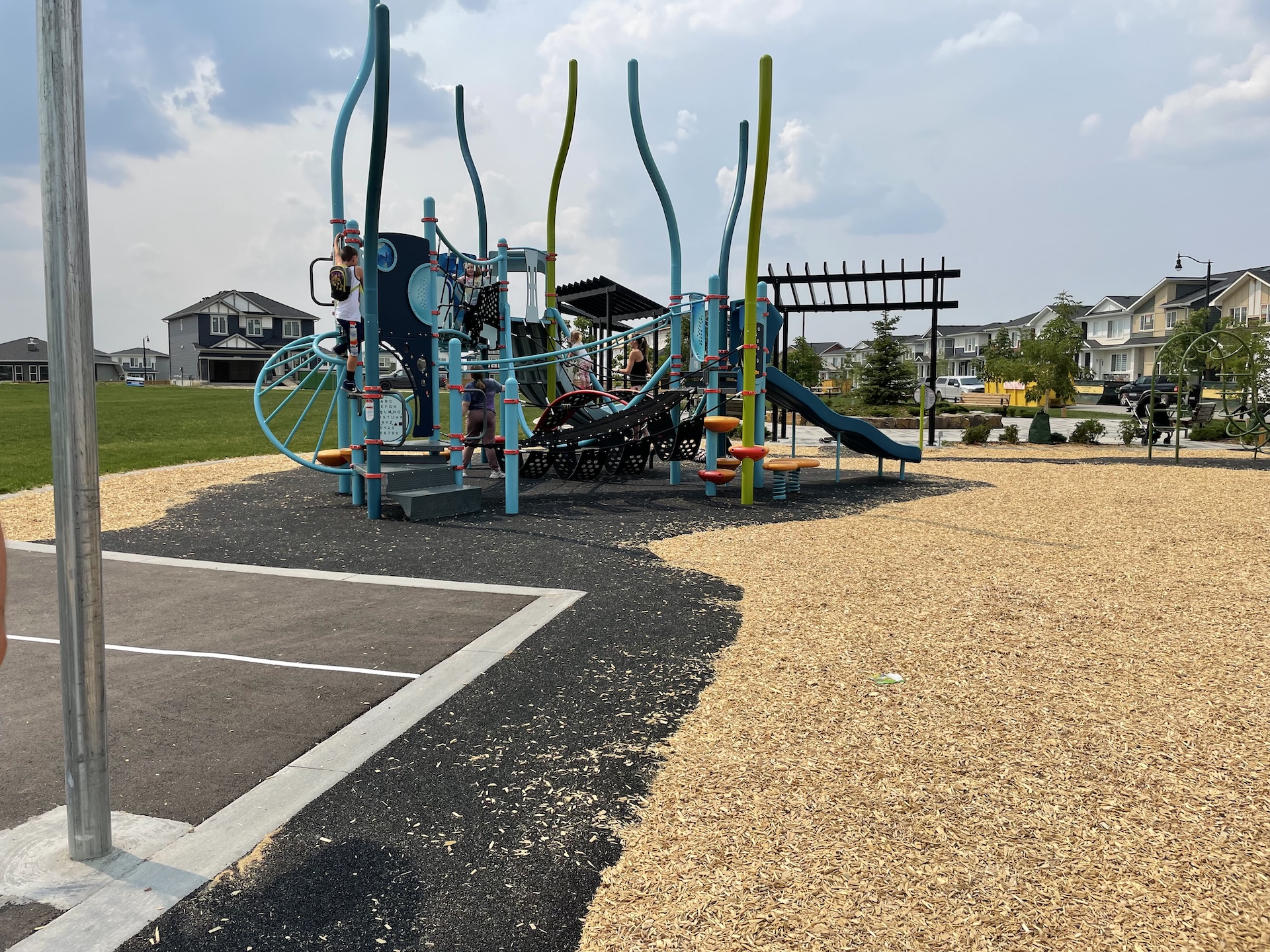 Modern playground in Dawson's Landing with climbing structures, slides, and colourful equipment on a wood chip surface, with houses in the background.